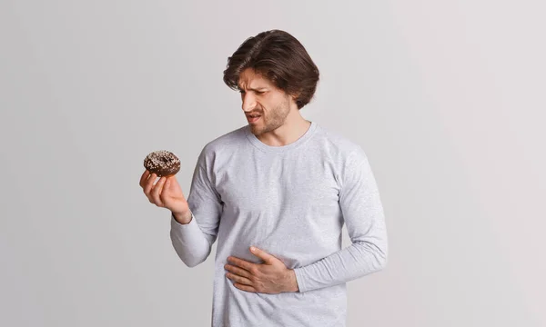 L'homme tient un beignet doux dans ses mains et le regarde avec douleur, serrant ses mains à l'estomac — Photo