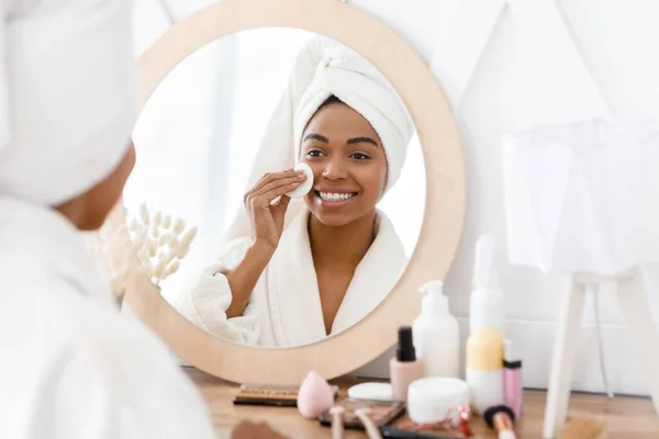 Rotina da Beleza. Menina africana bonita limpeza rosto com almofada de algodão em casa , — Fotografia de Stock