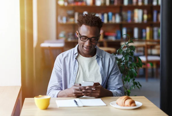 Felice uomo afroamericano utilizzando il telefono cellulare per l'apprendimento online in caffè urbano — Foto Stock