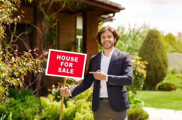 Immobilienmakler zeigt auf Schild mit der Aufschrift HAUS ZU VERKAUFEN vor schönem Gebäude im Freien — Stockfoto