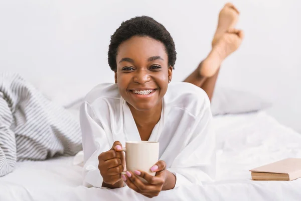 Inicio positivo del día y el café. Mujer acostada en la cama en albornoz y taza de celebración —  Fotos de Stock