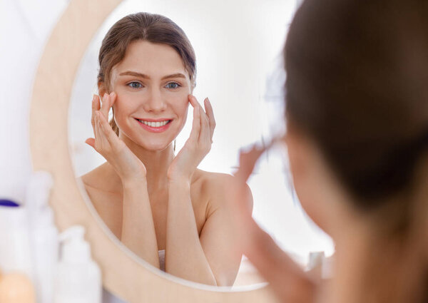 Beautiful woman looking at mirror and applying eye serum