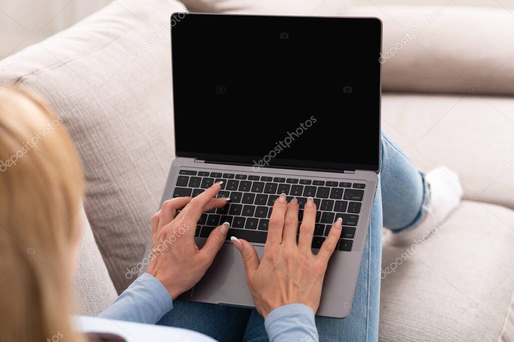 Work on couch. Woman is typing on laptop with blank screen, sitting on sofa
