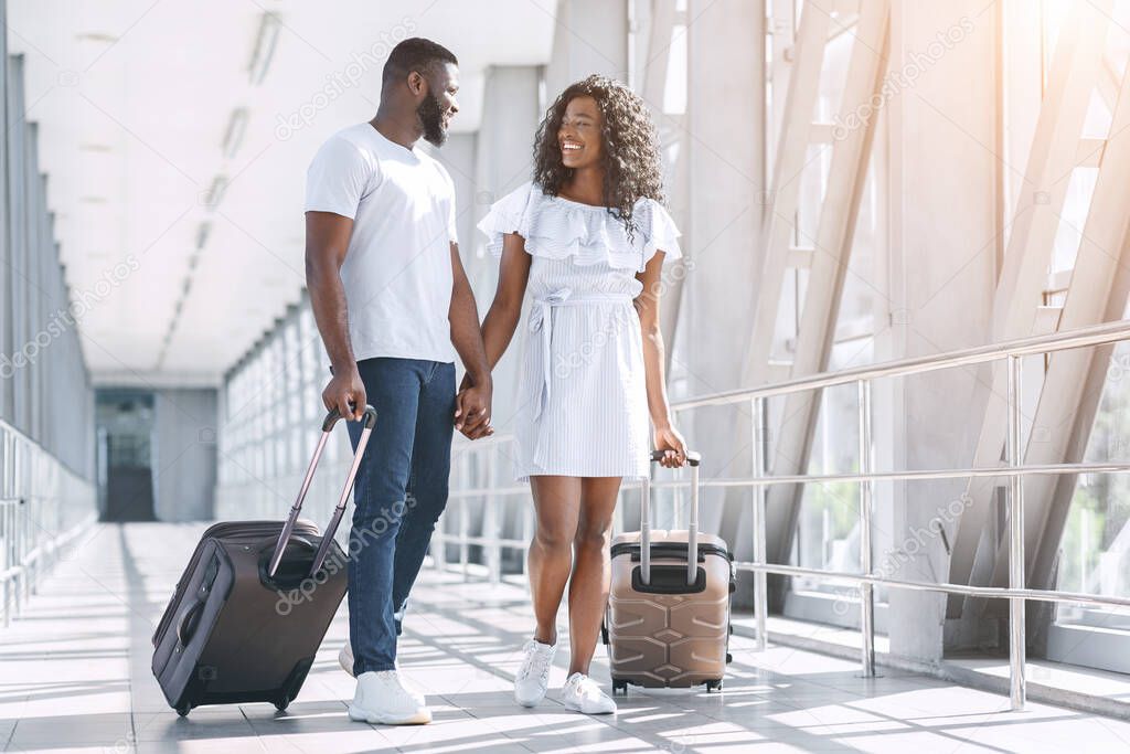 Affectionate Black Couple Enjoying Honeymoon Trip, Walking With Suitcases In Aiport