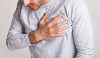 Stres ve sağlık konsepti. Genç adam göğüs ağrısı çekiyor ve eğiliyor.
