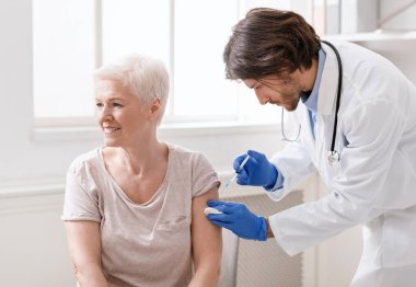 Doktor yaşlı kadın hastaya aşı yapıyor.