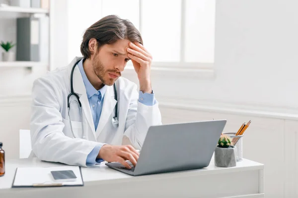 Endişeli erkek doktor dizüstü bilgisayardan kötü test sonuçlarına bakıyor. — Stok fotoğraf