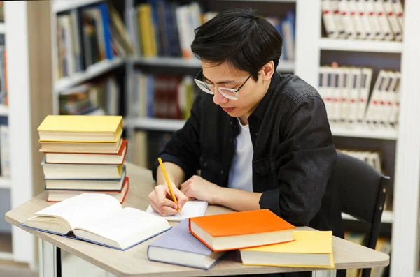 Asiático cara fazendo lição de casa sentado na mesa na biblioteca — Fotografia de Stock