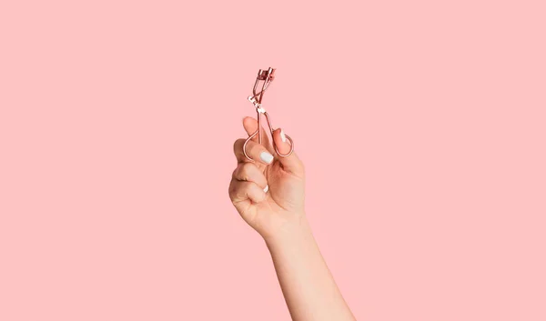 Szekrény kozmetikus kéz gazdaság szempilla curler rózsaszín háttér — Stock Fotó