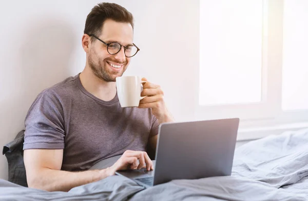 Mężczyzna Korzystanie Laptop Przeglądanie Internetu Siedząc w łóżku w domu — Zdjęcie stockowe