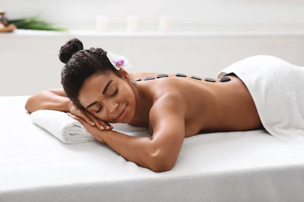 Afrikansk flicka liggande på spa salong, få varm sten massage — Stockfoto