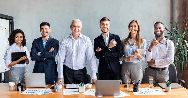 Coworkers sorridenti che posano vicino alla tabella nell'ufficio moderno, panorama — Foto Stock