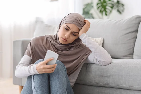 Depressionskonzept. Verärgerte Araberin sitzt zu Hause mit Smartphone auf dem Boden — Stockfoto