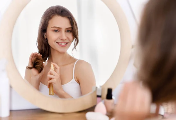 Jolie fille appliquant de l'huile capillaire, regardant miroir à la maison — Photo