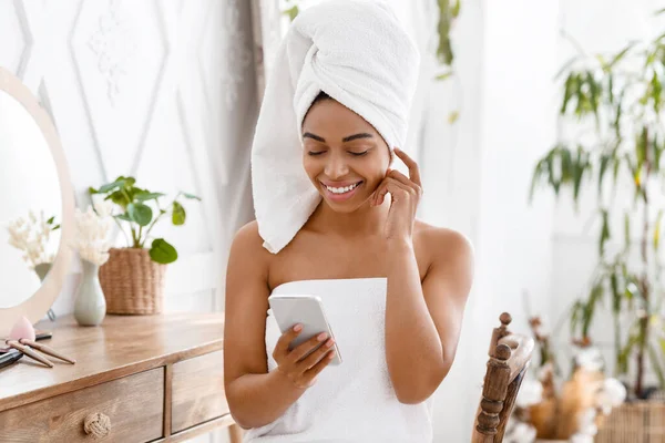 Klaar voor het afspraakje. zwart meisje verpakt in handdoek sms 'en op smartphone — Stockfoto