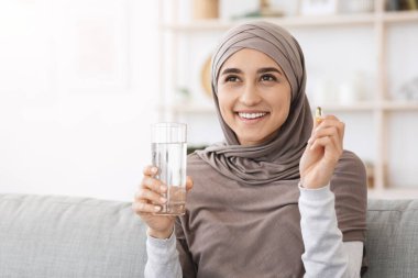Güzellik takviyesi. Mutlu Müslüman kadın evde vitamin kapsülü ve su alıyor.