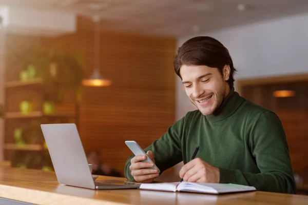 Freelancer trabajando en el proyecto en la cafetería, utilizando el ordenador portátil y el teléfono inteligente — Foto de Stock