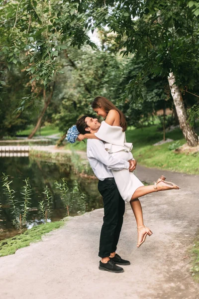 Sposo che solleva la sposa in piedi vicino al lago nel bellissimo parco, verticale — Foto Stock