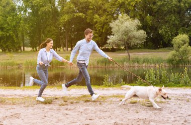 Heyecanlı çift ve av köpeği göl kenarında koşuyor.