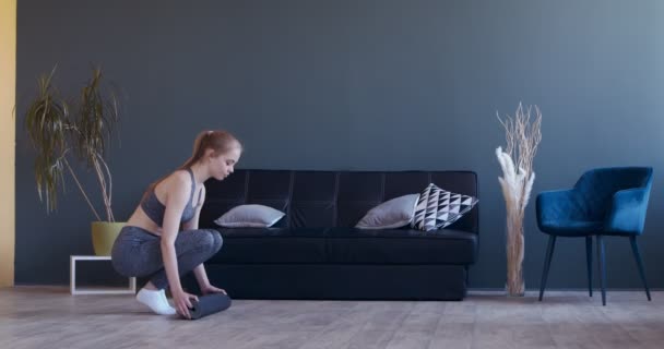 Fit vrouw ontvouwen mat voor het beoefenen van yoga thuis — Stockvideo