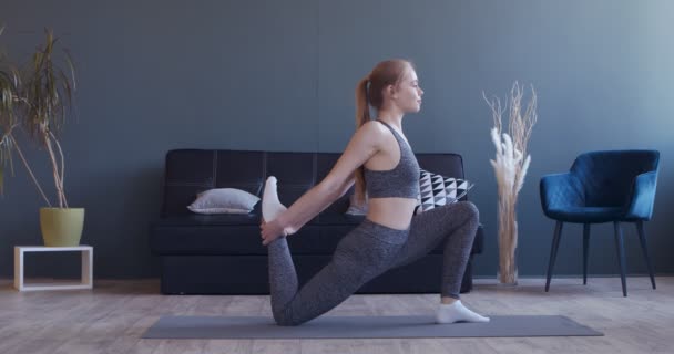 Ung kvinna sträcker på benen, övar pilates hemma — Stockvideo