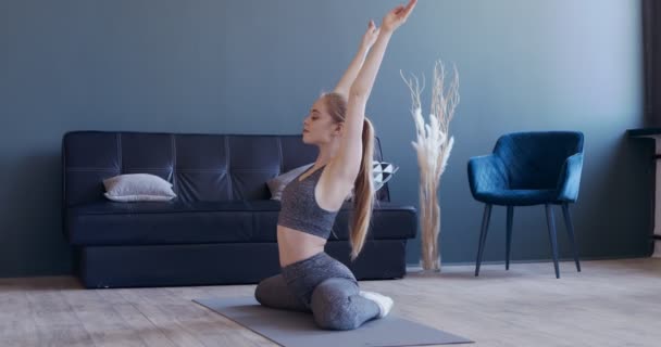 Menina esticando as costas, sentado no tapete de fitness em casa — Vídeo de Stock