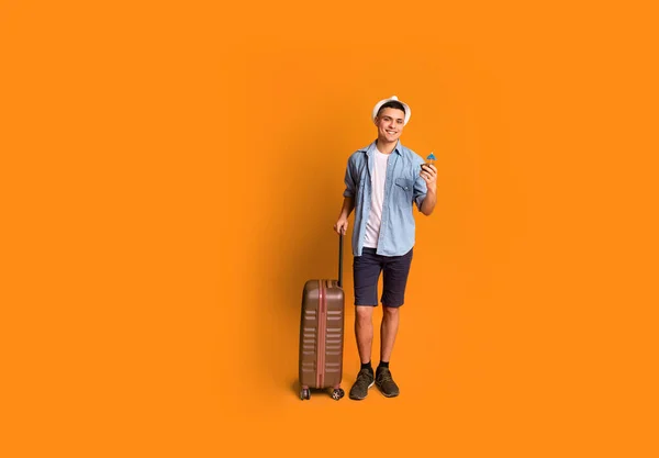 Happy tourist with suitcase holding cocktail, orange background