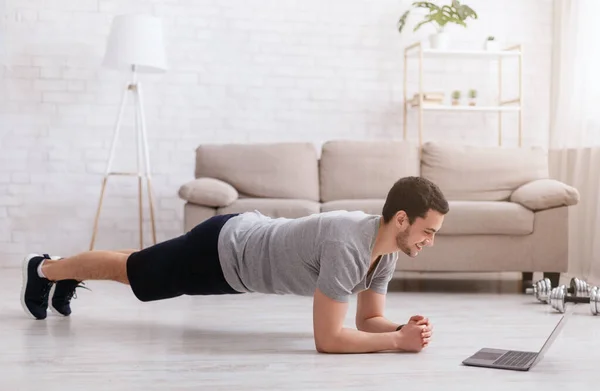 Entraîneur et sport en ligne. Jeune homme fait planche et regarde ordinateur portable — Photo