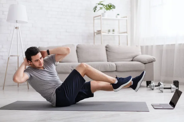 Sport and healthy lifestyle. Man does exercises for abdominal muscles and watches online training — Stock Photo, Image