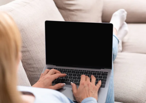 Arbeiten Sie online. Frau tippt auf Laptop mit leerem Bildschirm, liegt zu Hause auf Sofa, Schulterblick — Stockfoto