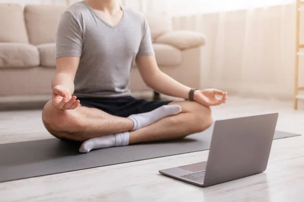 Nowoczesna lekcja jogi. Facet siedzący na podłodze w pozycji lotosu, przed laptopem — Zdjęcie stockowe