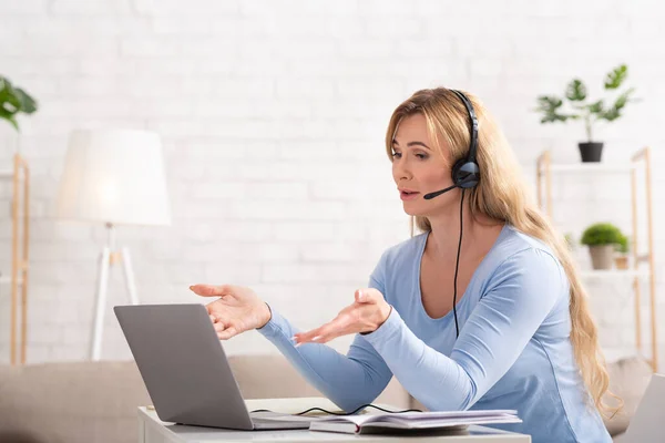 Reunião de negócios online. Mulher adulta com fone de ouvido se comunica com o cliente no laptop — Fotografia de Stock