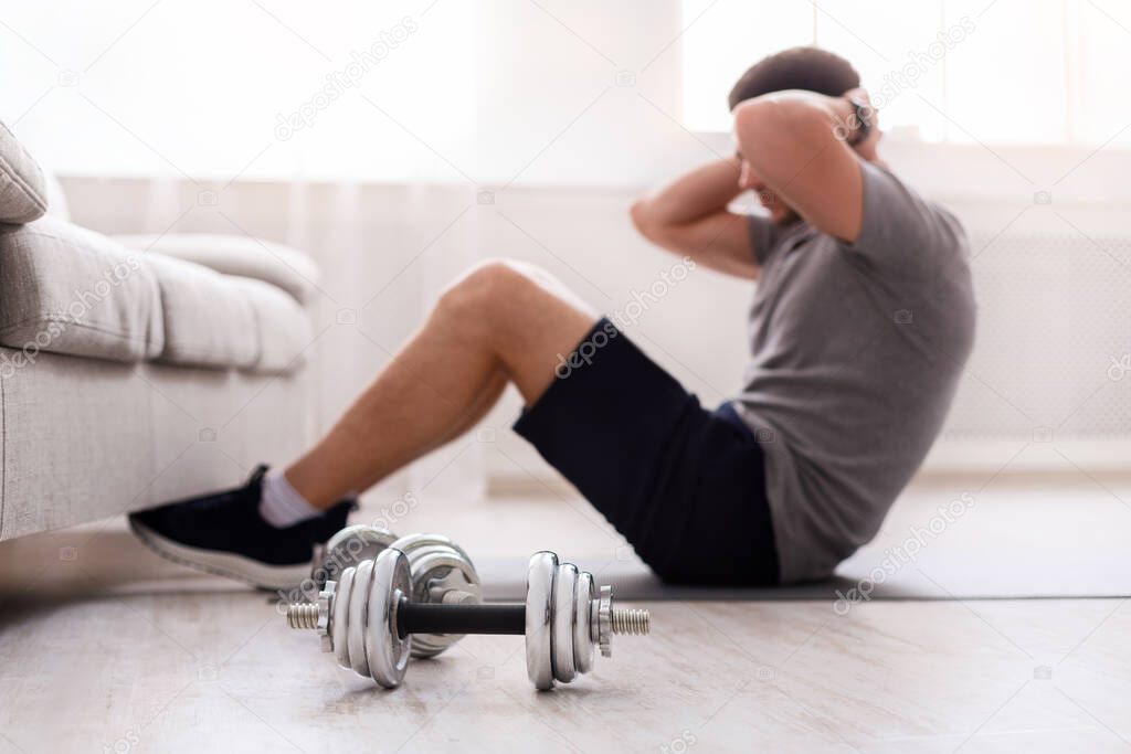 Guy does exercises for abs, shove his legs under couch. Dumbbells on floor, close up