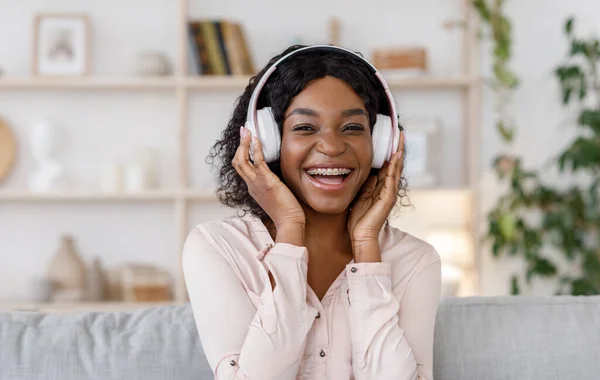Radosna czarna dziewczyna z aparatem słuchającym muzyki w bezprzewodowych słuchawkach w domu — Zdjęcie stockowe