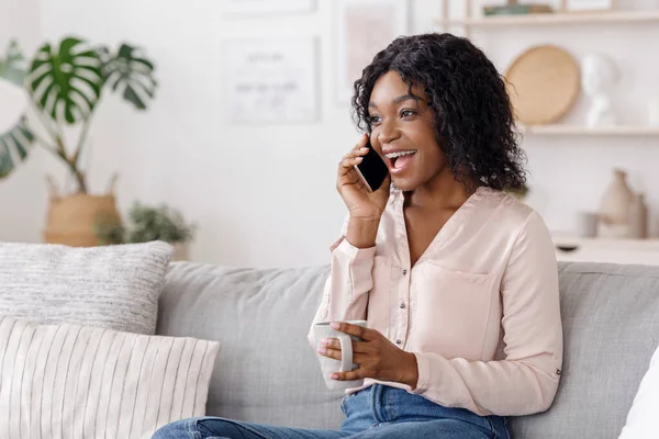 Spaar tijd thuis. Zwarte vrouw praten op mobiele telefoon en genieten van koffie — Stockfoto