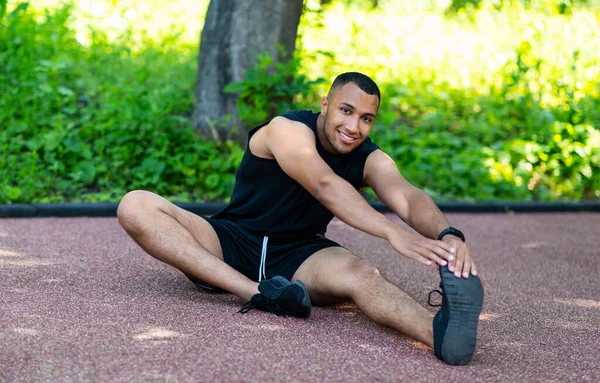 Bonito atleta afro-americano que se estende na pista de jogging no parque — Fotografia de Stock