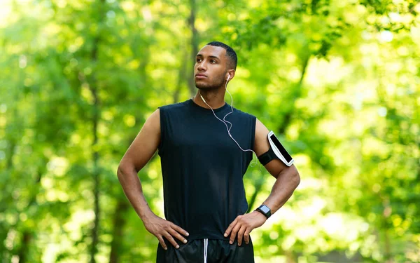 Hombre negro guapo con auriculares escuchando música durante su carrera matutina en el parque — Foto de Stock