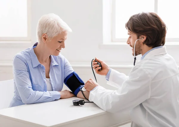 Klinikteki yaşlı kadının tansiyonunu ölçen doktor. — Stok fotoğraf