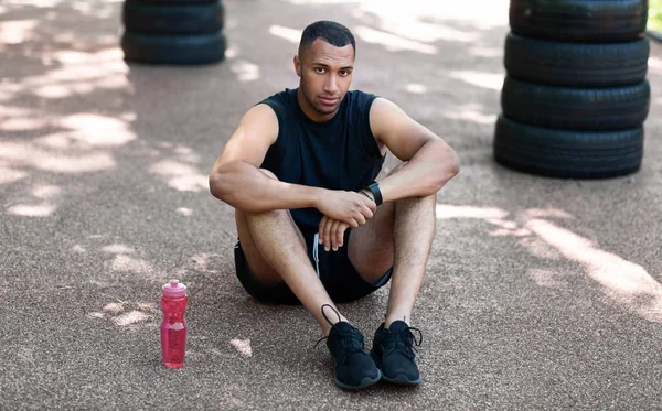 Hombre negro guapo sentado en pista de jogging en el parque, descansando después de su entrenamiento —  Fotos de Stock