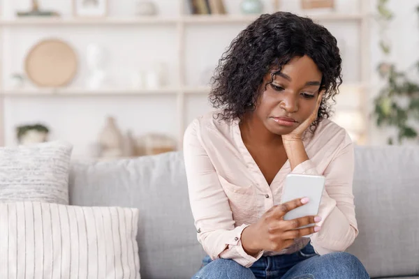 À espera da chamada dele. Mulher negra deprimida sentada com celular em casa — Fotografia de Stock