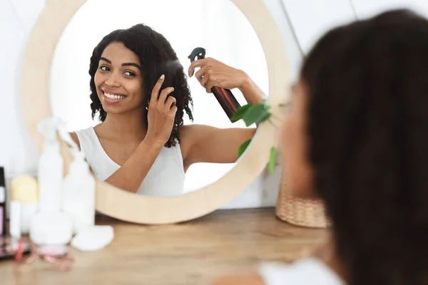 Menata rambut. Wanita kulit hitam yang cantik menggunakan semprotan rambut untuk menyisir Cermin Dekat Mudah — Stok Foto