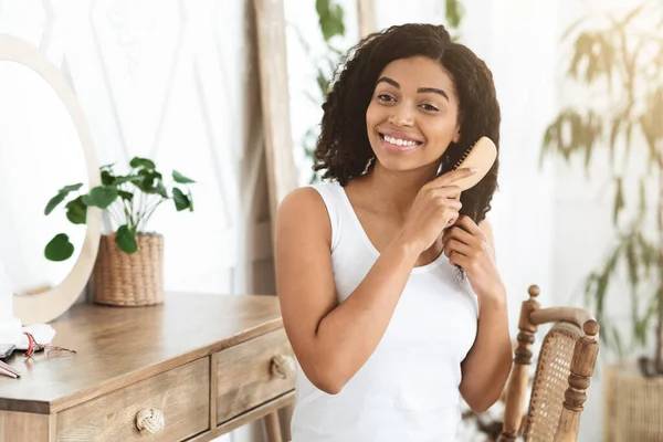 Mulher negra bonita penteando seu cabelo encaracolado, se preparando pela manhã — Fotografia de Stock