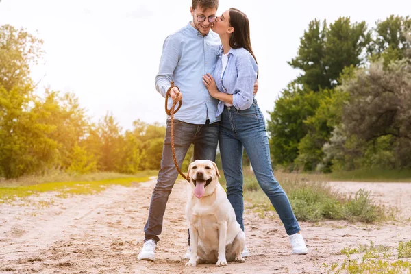 Porträtt av glada unga par gå hund och kyssas — Stockfoto