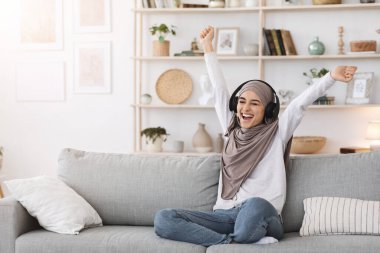 Enerji Haftasonu. Aşırı neşeli Müslüman kadın evde kablosuz kulaklıkla müzik dinliyor.