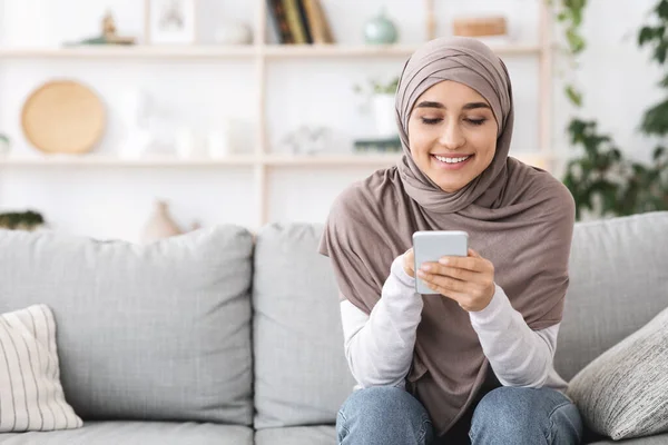 Glückliches muslimisches Mädchen mit Kopftuch entspannt mit Handy zu Hause — Stockfoto