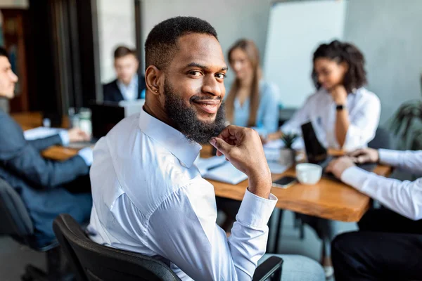 Empresário preto sorrindo para câmera sentado em reunião no escritório — Fotografia de Stock
