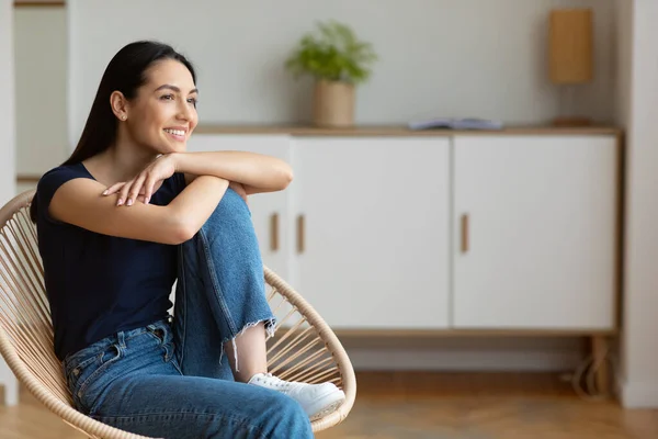 Gelukkig vrouw ontspannen zitten in gezellige moderne stoel thuis — Stockfoto