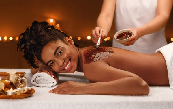 Massage therapist applying body mask on african lady back — Stock Photo, Image