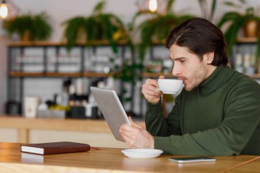Genç girişimci kahve içiyor ve dijital tablet kullanıyor.