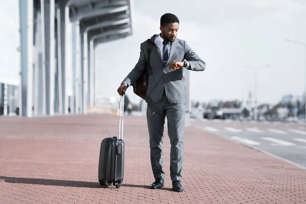 Afroamerikanischer Geschäftsmann checkt Zeit mit Koffer am Flughafen — Stockfoto